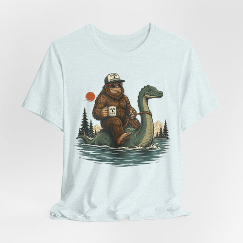 Heather ice blue unisex t-shirt with Bigfoot in Barely Outdoorsy trucker hat and sunglasses riding Loch Ness Monster on lake holding Lake Life mug graphic, Bella Canvas 3001
