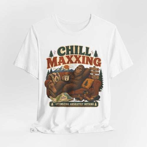 White unisex t-shirt with Bigfoot lounging on couch holding Peak Nah mug with trail map Maybe Tomorrow and signpost Effort Pass graphic reading Chill Maxxing Optimizing Absolutely Nothing, Bella Canvas 3001